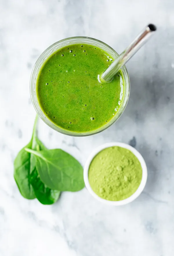 Overhead view of a green smoothie made with moringa and spinach, served in a clear glass with a stainless steel straw