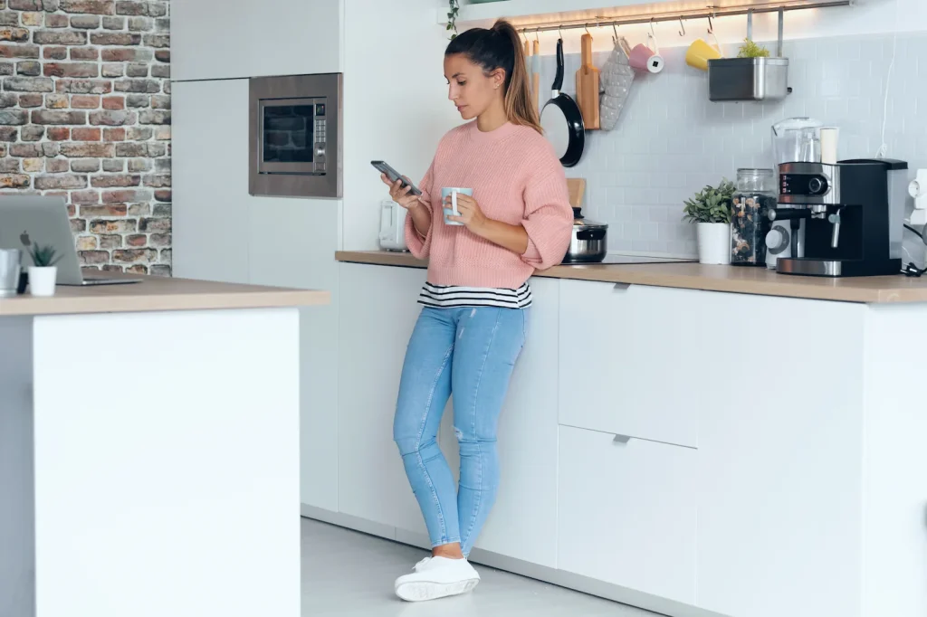 Young woman checking her smartphone while standing in a kitchen at home